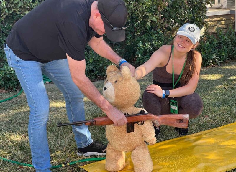 Allie Mitchell and Blair Clark help Ted exercise his right to “bear” arms. Image © Peacock